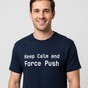 May include: A navy blue t-shirt with the text "Keep Calm and Force Push" in white. The shirt is being worn by a person smiling at the camera. The background is a solid light gray.