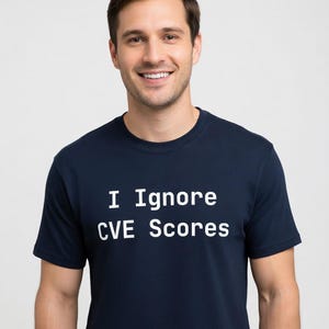 Op de afbeelding: Marineblauw t-shirt met de witte tekst "I Ignore CVE Scores". Het shirt is gemaakt van een zacht materiaal en is geschikt voor vrijetijdskleding. De persoon op de foto lacht.