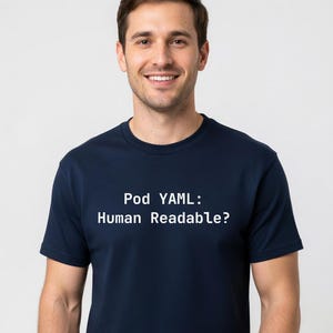 May include: A navy blue t-shirt with the text "Pod YAML: Human Readable?" in white. The shirt is worn by a person smiling at the camera. The t-shirt is a crew neck style.