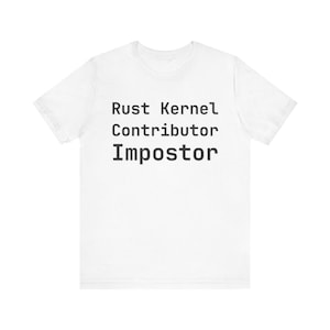 Op de afbeelding: Wit T-shirt met de tekst "Rust Kernel Contributor Impostor" in zwarte, schreefloze lettertype. Het shirt heeft korte mouwen en een ronde hals, gemaakt van een zacht materiaal.