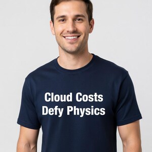 May include: A navy blue t-shirt with the white text "Cloud Costs Defy Physics." The t-shirt is a crew neck style and is being worn by a person smiling at the camera.