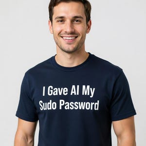 May include: Navy blue t-shirt with the white text "I Gave AI My Sudo Password". The shirt is a crew neck style.