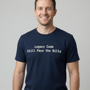 May include: A navy blue short-sleeved t-shirt featuring the white text Legacy Code Still Pays the Bills printed across the chest. The garment has a classic crew neckline and a standard fit, providing a clean and straightforward appearance.