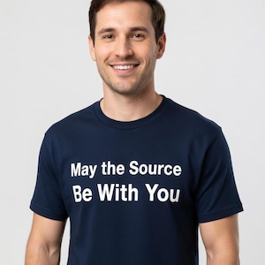 May include: A navy blue t-shirt with the white text "May the Source Be With You." The shirt is a crew neck style and is being worn by a person.