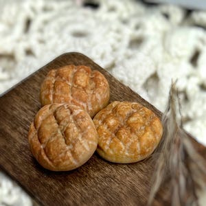 May include: Three golden brown bread rolls with a criss-cross pattern on a wooden cutting board.