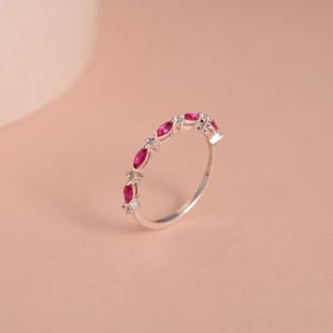 May include: A silver band ring with a row of small, oval-shaped red gemstones and clear, round gemstones.