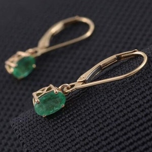 May include: A pair of gold drop earrings featuring emerald green gemstones. The earrings have a lever back fastening.