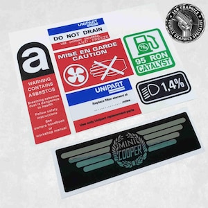 Op de afbeelding: Een set van acht stickers voor een Mini Cooper auto. De stickers zijn zwart, wit, rood, groen en blauw. De stickers bevatten waarschuwingen over asbest, instructies voor het vervangen van een filterelement en een waarschuwing over het gebruik van antivries. De stickers bevatten ook een Mini Cooper logo met vleugels en de tekst "Mini Cooper".