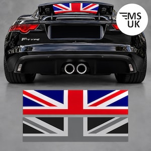 Może przedstawiać: Czarny samochód sportowy Jaguar F-Type widziany od tyłu, z naklejką Union Jack umieszczoną na spojlerze. Poniżej samochodu widoczne są dwie prostokątne naklejki: jedna w kolorach czerwonym, białym i niebieskim oraz druga w odcieniach szarości i czerni.