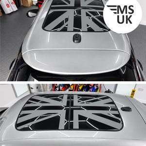 May include: A silver car roof featuring a black panoramic sunroof panel with a grey Union Jack flag decal overlaid on the glass. The decal incorporates a white hexagonal honeycomb pattern within the flag design. A black shark fin antenna is present.