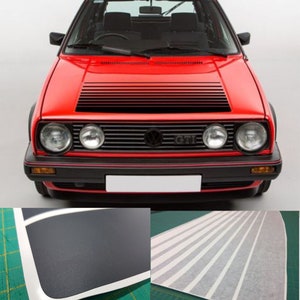 Könnte beinhalten: Ein roter Volkswagen GTI mit schwarzen Zierleisten und einem schwarzen Kühlergrill. Das Auto hat einen schwarzen Streifen auf der Motorhaube und einen schwarz-weißen Streifenaufkleber an der Seite.