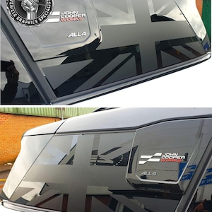 Op de afbeelding: Een zwarte auto met een Union Jack-vlag sticker op het achterraam. De sticker is zwart-wit en wordt gedeeltelijk bedekt door het achterraam van de auto. De auto heeft ook een "John Cooper Works" badge op de achterdeur.