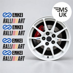 Op de afbeelding: Een wit lichtmetalen wiel met meerdere spaken, voorzien van een zwarte naafdop met Mitsubishi-logo, een rode Brembo-remklauw en Enkei en Ralliart-branding. Links staan vier sets Enkei Ralliart-stickers, met daarboven een MS UK-logo.