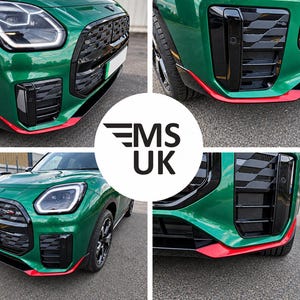 Può includere: La parte anteriore di un veicolo verde con una griglia nera dal motivo geometrico, fari a LED e un accento rosso sul paraurti inferiore. Il logo circolare centrale mostra il testo MS UK con una grafica ad ala stilizzata sopra le lettere MS.