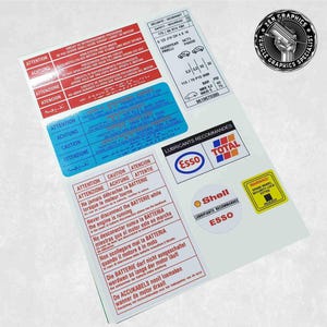 Può includere: Un foglio di adesivi bianco con etichette di avvertenza rosse, blu e gialle. Le etichette contengono istruzioni di sicurezza in più lingue, tra cui inglese, francese, tedesco, spagnolo, italiano e polacco. Le etichette includono anche informazioni sui lubrificanti raccomandati, come Esso e Total. Il foglio include anche un'etichetta di avvertenza su un bloccaggio di sicurezza per la ruota di scorta.