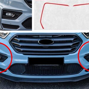 May include: A blue Ford Transit Connect with a black grille and a black front bumper. The front bumper has two round fog lights on either side of the grille. The Ford logo is visible on the grille.