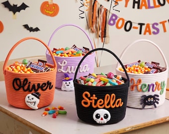 May include: Four round rope baskets for Halloween candy, each featuring a unique color and personalized name. The orange basket says Oliver, the purple says Luna, the black says Stella, and the white says Henry, with festive character appliques.