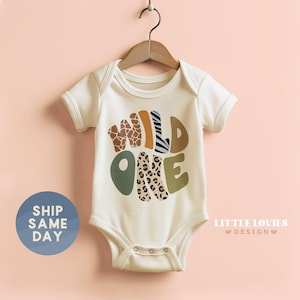 a baby laying on a bed wearing a wild one onesie