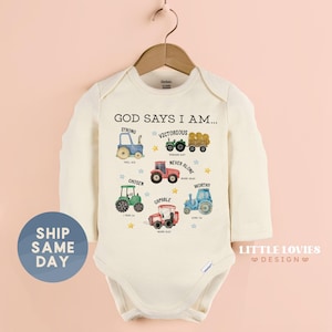 May include: Cream-colored baby onesie with long sleeves, featuring colorful tractor illustrations and the text "GOD SAYS I AM..." with inspirational words. The design includes a blue circle with the text "SHIP SAME DAY".