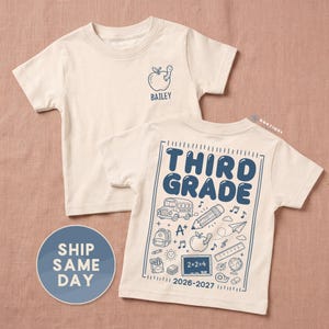 May include: A cream-colored short-sleeve t-shirt featuring a blue graphic of an apple with a worm and the name BAILEY on the front. The back displays a large blue design with the text THIRD GRADE, 2026-2027, and various school-themed icons.
