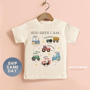 A white t-shirt with a graphic design featuring various farm vehicles and the text "GOD SAYS I AM... STRONG VICTOROUS NEVER ALONE CHOSEN WONDERFUL MARKETPLACE Tractor".
