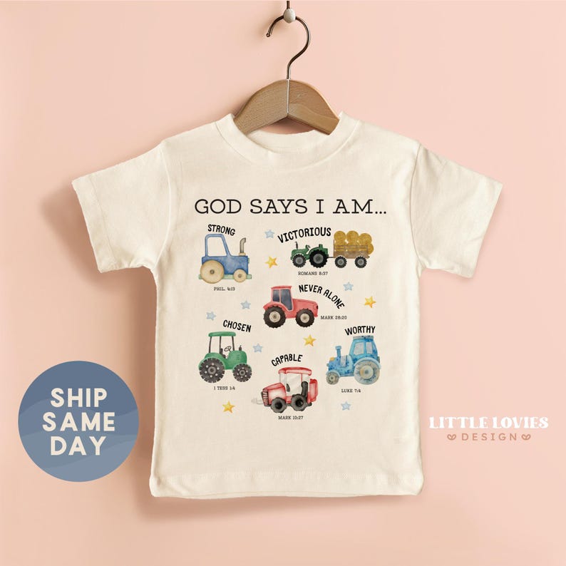 A white t-shirt with a graphic design featuring various farm vehicles and the text "GOD SAYS I AM... STRONG VICTOROUS NEVER ALONE CHOSEN WONDERFUL MARKETPLACE Tractor".