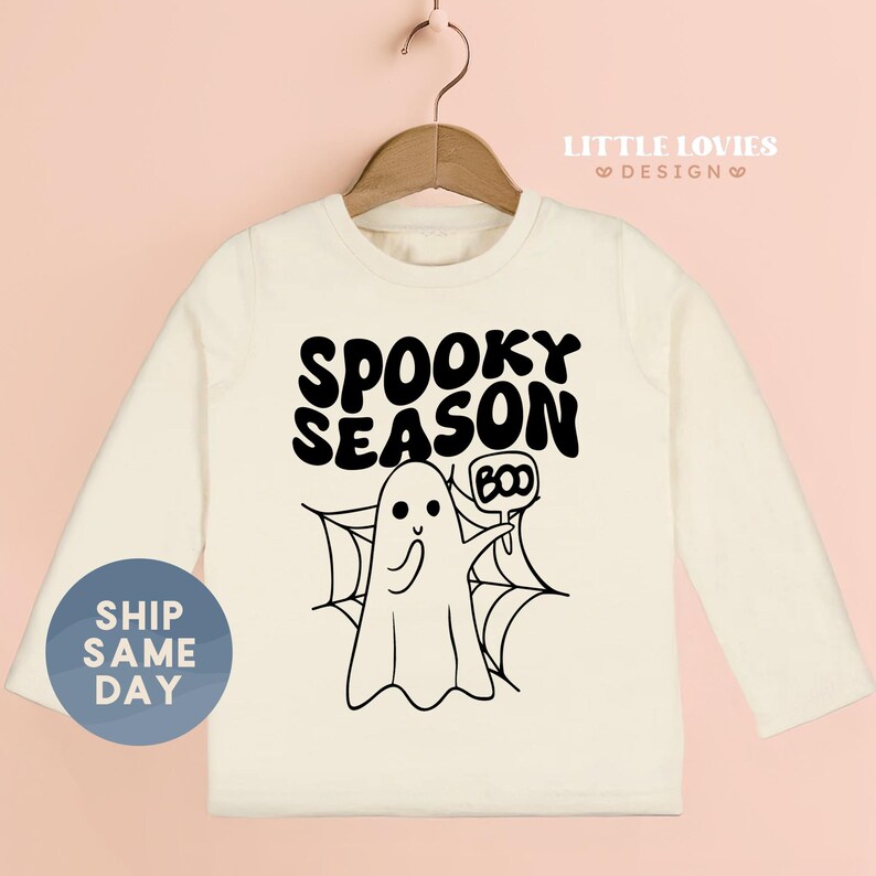 A white long-sleeved t-shirt with a graphic design featuring a ghost character and the text "SPOKEY SEASON BOO" printed on it.
