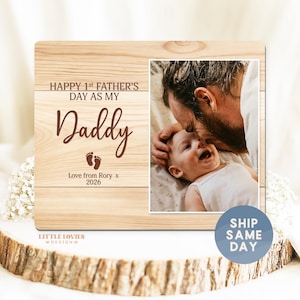 May include: A wooden photo frame with a picture of a baby and a man kissing the baby's head. The frame has the text "HAPPY 1st FATHER'S DAY AS MY Daddy" and "Love from Rory x 2026".