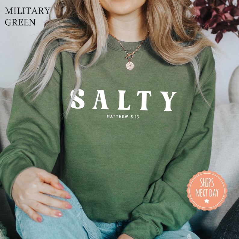 a woman sitting on a couch wearing a military green sweatshirt
