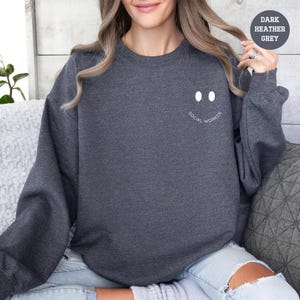 a woman sitting on a couch wearing a dark sweatshirt with a smiley face drawn on