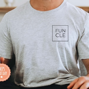 May include: A gray t-shirt with a black square on the front that says "FUN CLE".