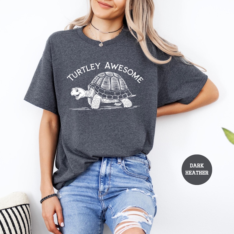 A woman wearing a gray t-shirt with a graphic of a turtle and the text "TURTLEY AWESOME" printed on it, paired with distressed blue jeans.