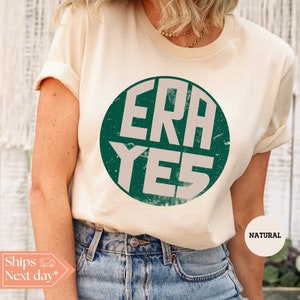 May include: A cream colored t-shirt with a green circle graphic that says "ERA YES" in white letters. The shirt is made of a soft, comfortable material and is perfect for everyday wear.