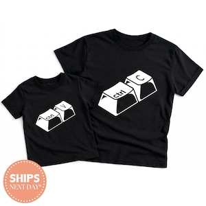 May include: Black t-shirts with white keyboard key graphics. One shirt displays "ctrl" and "V" keys, the other shows "ctrl" and "C" keys. The shirts are likely for a parent and child or a matching set.