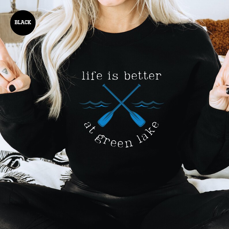 a woman sitting on a bed with a black shirt that says life is better green