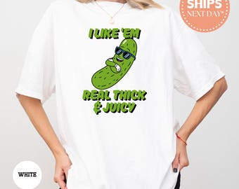 May include: White t-shirt with a green cartoon pickle wearing sunglasses and the text "I like 'em real thick & juicy".