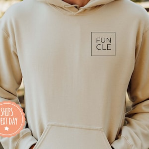 May include: A beige hoodie with a black square on the front that says "FUN CLE" in all caps.