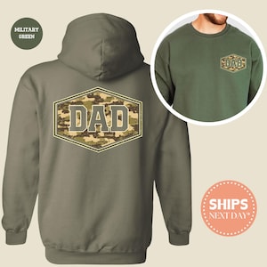 May include: Military green hoodie with a camouflage "DAD" design on the back. The design is in a hexagonal shape with a light brown border. A matching crew neck sweatshirt with the same design is also shown.