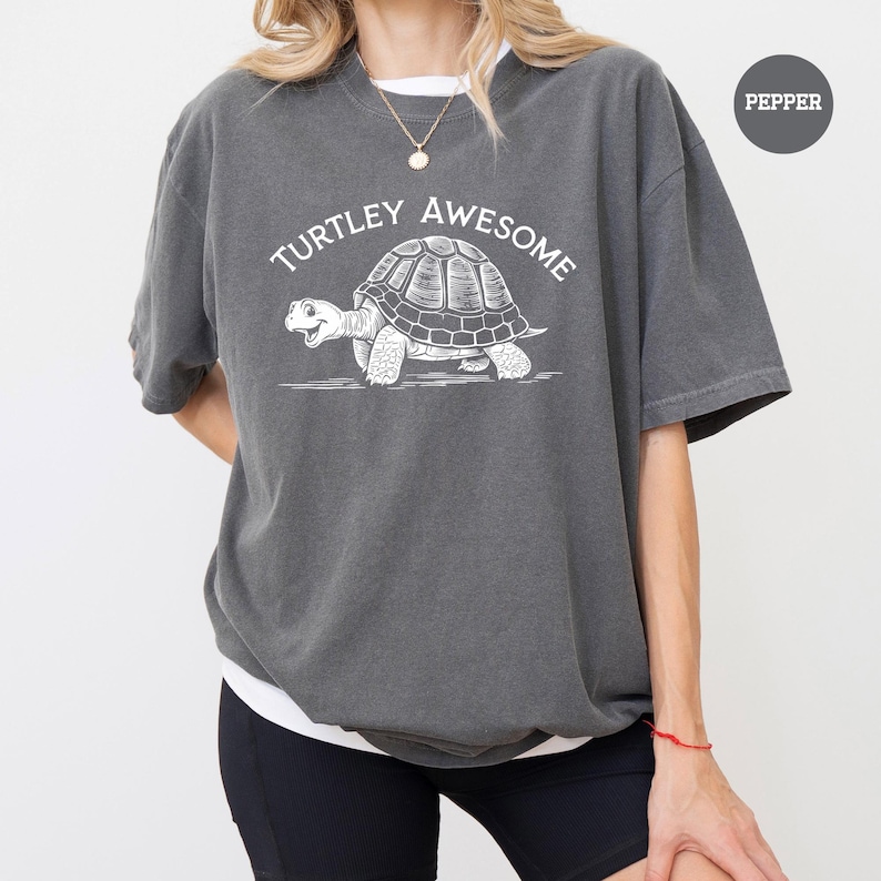 A person wearing a gray t-shirt with a graphic of a turtle and the text "TURTLEY AWESOME" printed on it.