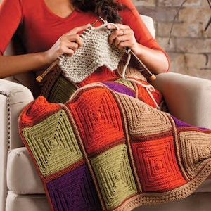 以下が含まれることがあります： オレンジ、グリーン、パープル、ブラウンの色合いの正方形でできたカラフルな編み物の毛布。毛布は椅子に座っている人が編んでいます。