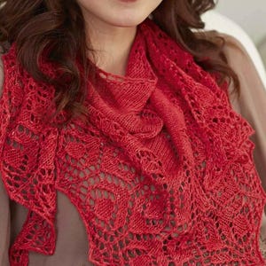 Puede incluir: Un chal de punto rojo vibrante con intrincados patrones calados. El chal está drapeado alrededor de los hombros, mostrando su diseño texturizado y su color intenso. El calado crea una sensación delicada y aireada, perfecta para añadir un toque de elegancia.