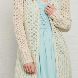 May include: Cream-colored, open-front cardigan with a delicate, open-weave design. The long-sleeved sweater features a knee-length cut and ribbed cuffs and pockets. The cardigan is worn over a light blue dress.