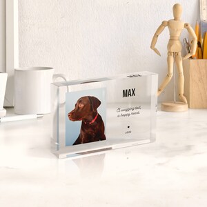 May include: A clear acrylic block with a photo of a brown dog with a red collar. The text "MAX" is printed on the block, along with the quote "A wagging tail, a happy heart." and the year "2022".