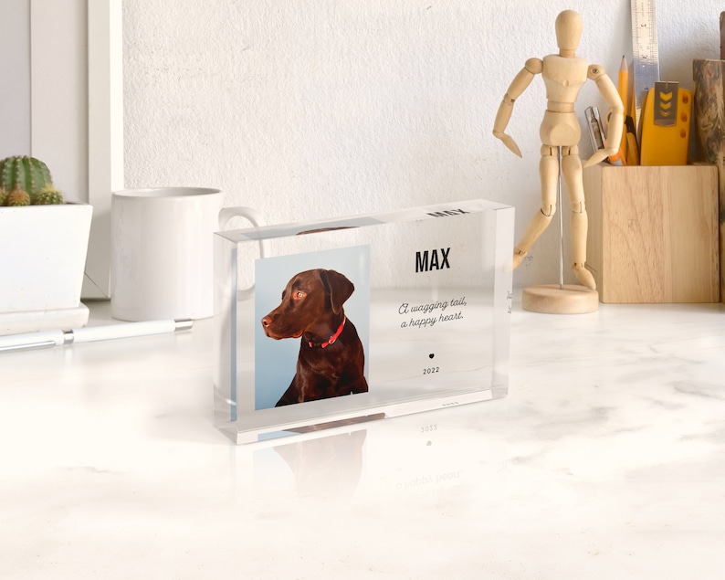 May include: A clear acrylic block with a photo of a brown dog with a red collar. The text "MAX" is printed on the block, along with the quote "A wagging tail, a happy heart." and the year "2022".