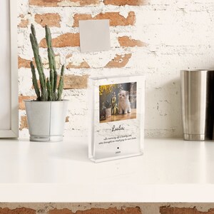 May include: A clear acrylic photo block with a picture of a white kitten sitting on a floral background. The text "Lulu" is written in black cursive font with the message "With memory of a loving soul who brought so much joy to our lives." and the year "2020" below.