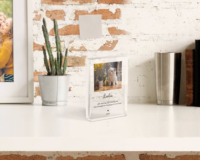 May include: A clear acrylic photo block with a picture of a white kitten sitting on a floral background. The text "Lulu" is written in black cursive font with the message "With memory of a loving soul who brought so much joy to our lives." and the year "2020" below.