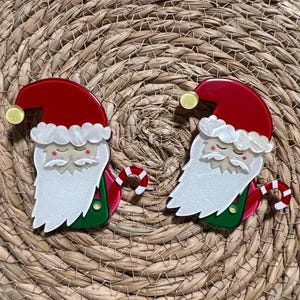 May include: Two red and white Santa Claus ornaments with candy cane accents. The ornaments are made of acrylic and have a glitter finish.