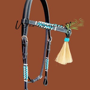 May include: Black leather horse bridle with white stitching and turquoise and white zigzag accents. Features a decorative tassel and a turquoise accent piece. The bridle is designed for equestrian use.