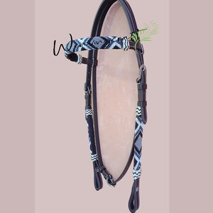 May include: A horse bridle with a decorative beaded browband and cheek pieces. The bridle is made of dark brown leather with white stitching and silver-toned hardware. The beaded sections feature a geometric pattern in black, white, and gray.