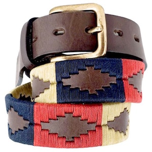 May include: A brown leather belt with a brass buckle and a woven strap with red, blue, and beige stripes. The strap has a brown leather patch with a woven design.